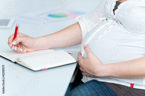 Photo: schwangere frau schreibt etwas in ihren kalender schwangere frau schreibt etwas in ihren kalender