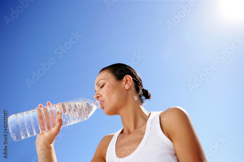 Photo: Woman drinking a bottle of water against a blue sky Woman drinking a bottle of water against a blue sky