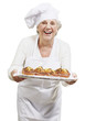 Photo: senior woman cook holding a tray with muffins against a white ba senior woman cook holding a tray with muffins against a white ba