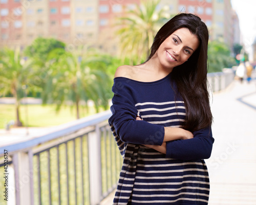 Photo: portrait of young woman with arms crossed against a park portrait of young woman with arms crossed against a park