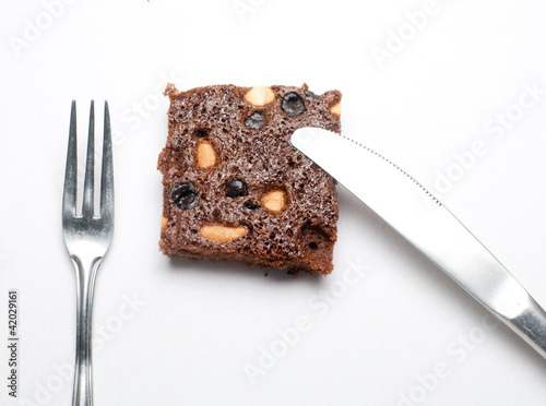 Photo: Piece of brownie with fork and knife on white isolated backgroun Piece of brownie with fork and knife on white isolated backgroun