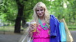 Happy woman with shoping bags walking in park, steadicam shot