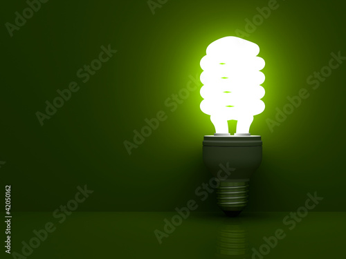 Photo: Energy saving light bulb glowing on green Energy saving light bulb glowing on green