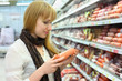 Foto: Blonde girl wearing scarf chooses sausage in large store Blonde girl wearing scarf chooses sausage in large store