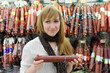 Foto: Smiling girl wearing scarf chooses sausage in large store Smiling girl wearing scarf chooses sausage in large store