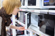 Blonde girl wearing scarf opens microwave in shop