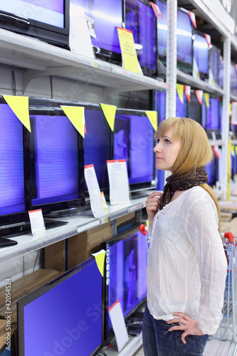 Photo: Blonde girl wearing scarf looks at plasma TVs in supermarket Blonde girl wearing scarf looks at plasma TVs in supermarket
