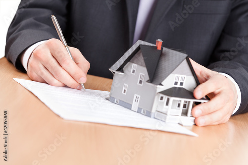 Foto: Business man signs contract behind household architectural model Business man signs contract behind household architectural model