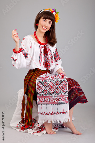 Foto: Attractive woman wears Ukrainian national dress is sewing Attractive woman wears Ukrainian national dress is sewing