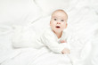 Happy active baby lying on stomach over white bed.  Three month