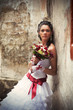 Photo: Bride with bouquet leaning against the wall of old building Bride with bouquet leaning against the wall of old building