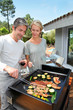 Couple in garden cooking meat on barbecue