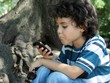 Beautiful curly child playing with cellphone sitting in the park