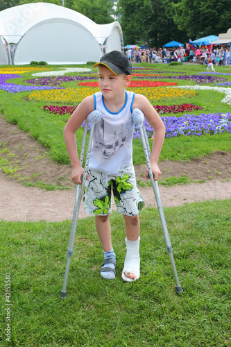 Foto: Sad boy on crutches in beautiful summer park; leg in cast Sad boy on crutches in beautiful summer park; leg in cast