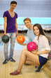 Two young men and girl with balls in bowling club;