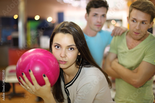 Photo: Woman prepares to throw of ball in bowling; two men look at her; Woman prepares to throw of ball in bowling; two men look at her;
