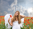 Angel girl in field of red poppies with white feather wings