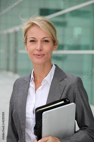 Photo: Mature businesswoman standing in front of modern building Mature businesswoman standing in front of modern building