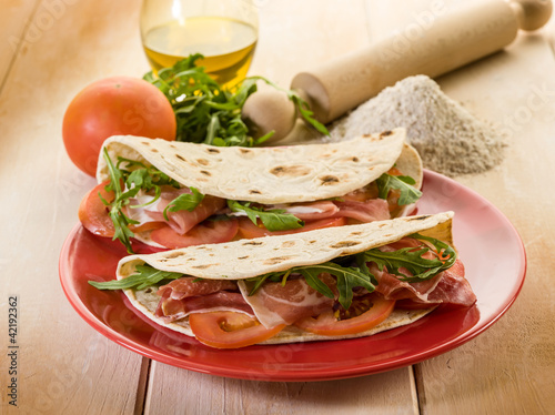 Photo: piadina with ham arugula and tomatoes, typical italian sandwich piadina with ham arugula and tomatoes, typical italian sandwich