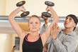 junge Frau beim Hanteltraining mit Trainer im Kraftraum