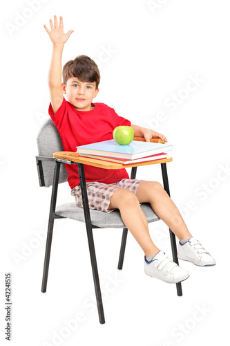 Foto: A schoolboy seated in a chair raising his hand A schoolboy seated in a chair raising his hand