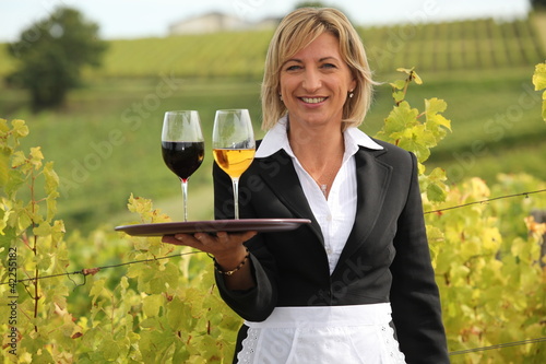 Photo: Woman serving red and white wine in a vineyard Woman serving red and white wine in a vineyard
