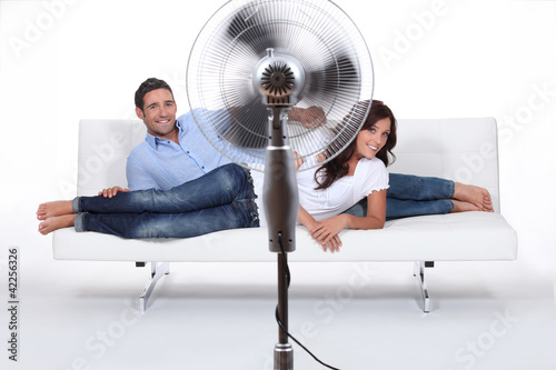 Photo: Man and woman laid on a sofa being ventilated by fan Man and woman laid on a sofa being ventilated by fan