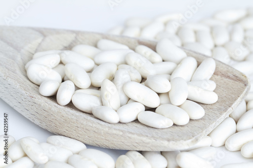 Photo: White beans on wooden spoon and a white background White beans on wooden spoon and a white background