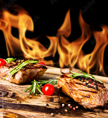 Foto: Grilled beef steaks with flames on background Grilled beef steaks with flames on background