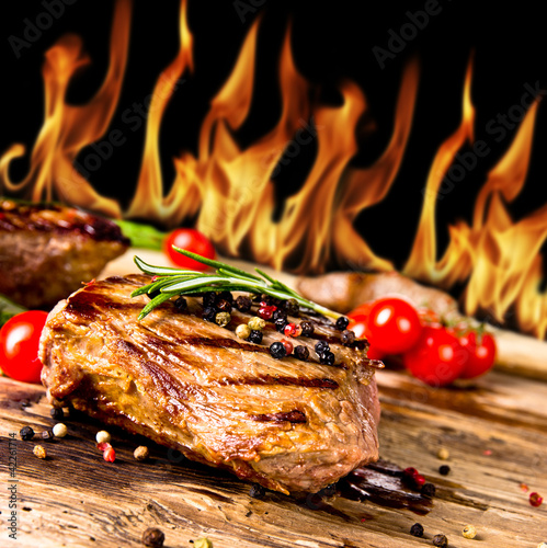  Grilled beef steaks with flames on background