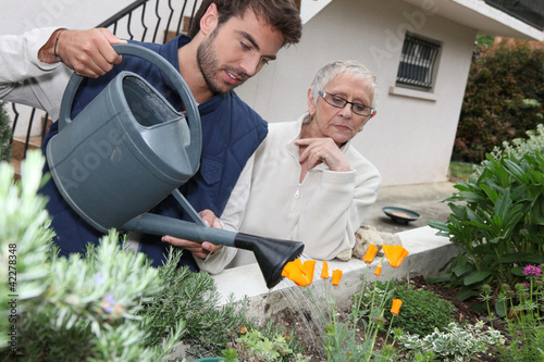 Photo: young man watering plants with older woman young man watering plants with older woman