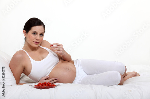 Photo: Pregnant woman laying on bed eating strawberries Pregnant woman laying on bed eating strawberries