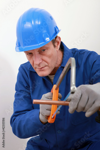 Photo: A tradesman using a saw to cut a copper tube A tradesman using a saw to cut a copper tube