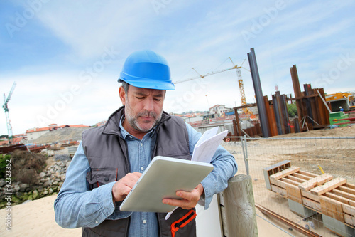 Foto: Construction manager controlling building site with plan Construction manager controlling building site with plan