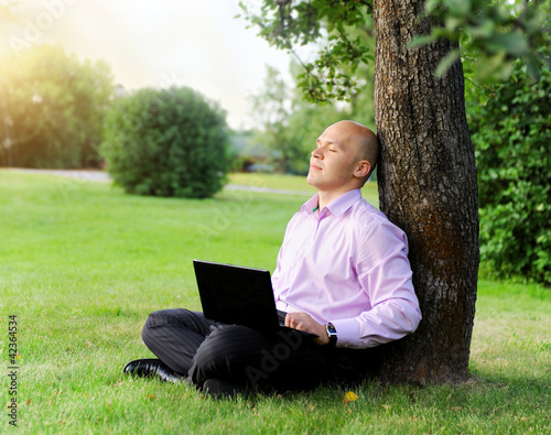 Photo: Businessman with laptop sitting near a tree Businessman with laptop sitting near a tree