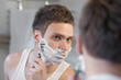 Photo: Young man shaving with razor shave looking in a mirror Young man shaving with razor shave looking in a mirror