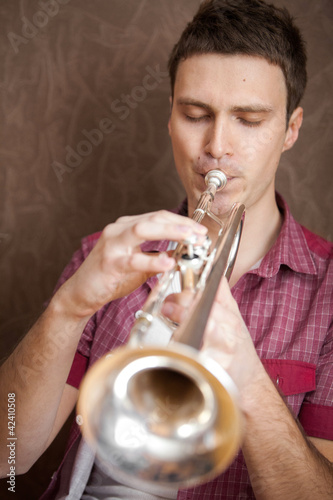 Photo: Handsome man playing on a silver trumpet Handsome man playing on a silver trumpet