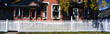 Photo: This is a more detailed look at a typical American home. It has a white picket fence in front with curtains in the window and a small gable over the entryway front door. Green-leafed trees line the side of the house. This is a more detailed look at a typical American home. It has a white picket fence in front with curtains in the window and a small gable over the entryway front door. Green-leafed trees line the side of the house.