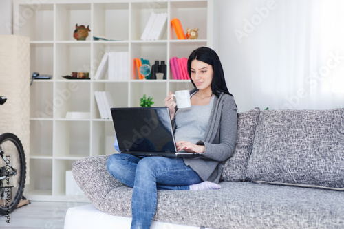 Photo: Woman holding a mug while using a laptop Woman holding a mug while using a laptop