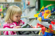 Photo: Adorable girl look to toys sit in shopping cart in supermarket Adorable girl look to toys sit in shopping cart in supermarket