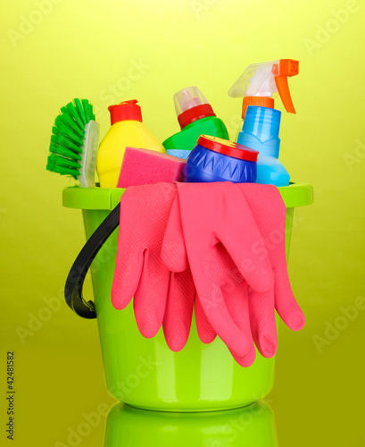 Photo: Bucket with cleaning items on green background Bucket with cleaning items on green background