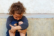 poor, sad little child girl sitting against the concrete wall