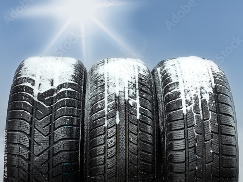 Foto: Three snowy winter tyres in front of blue sky with sunlights Three snowy winter tyres in front of blue sky with sunlights