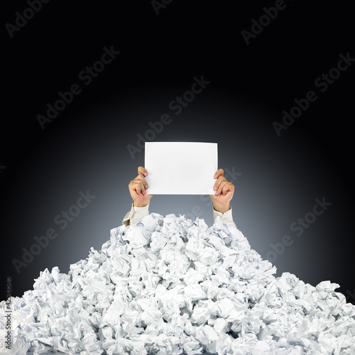 Photo: Person under crumpled pile of papers with hand holding a help si Person under crumpled pile of papers with hand holding a help si