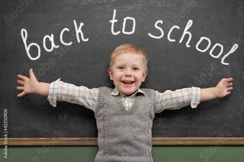 Photo: Cheerful smiling child stands at the blackboard. Looking at came Cheerful smiling child stands at the blackboard. Looking at came