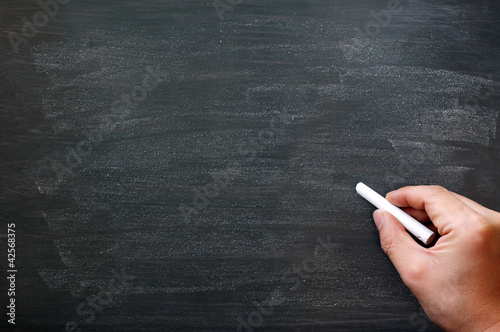 Photo: Smudged blackboard background with a hand holding chalk writing. Smudged blackboard background with a hand holding chalk writing.