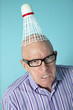 Portrait of angry senior man with shuttlecock on head over colored background