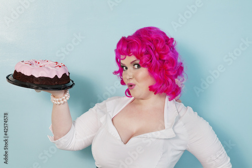 Photo: Portrait of happy woman showing cake over colored background Portrait of happy woman showing cake over colored background