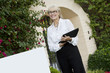 Photo: Cheerful senior woman standing by sign board with clipboard while looking away Cheerful senior woman standing by sign board with clipboard while looking away