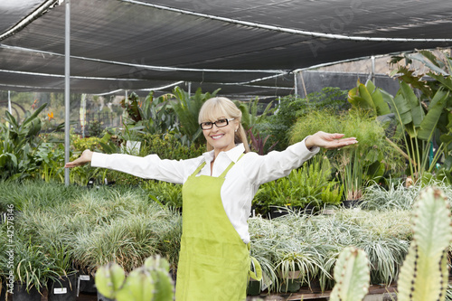 Photo: Portrait of a senior woman standing with arms outstretched in garden center Portrait of a senior woman standing with arms outstretched in garden center